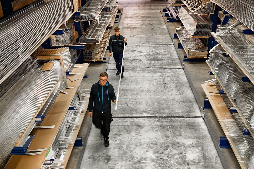 Zwei Auszubildende laufen durch das Aluminium-Lager von TS Aluminium und transportieren Profile.