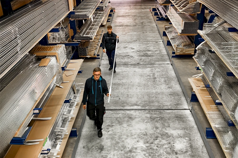 Zwei Auszubildende laufen durch das Aluminium-Lager von TS Aluminium und transportieren Profile.