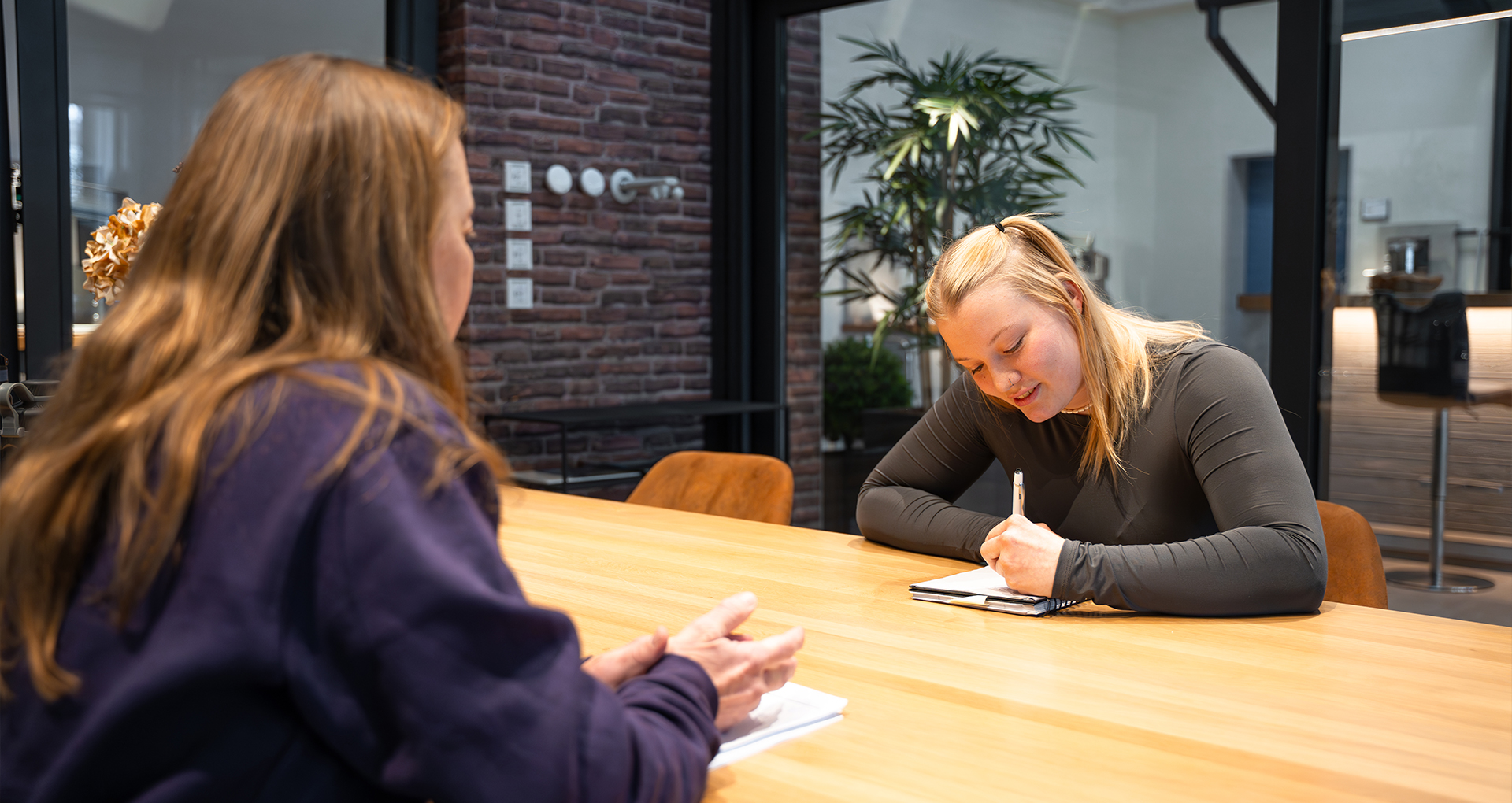 Schülerin im Gespräch mit Ausbilderin bei einem Bewerbungsgespräch oder Praktikumsfeedback im modernen Besprechungsraum.