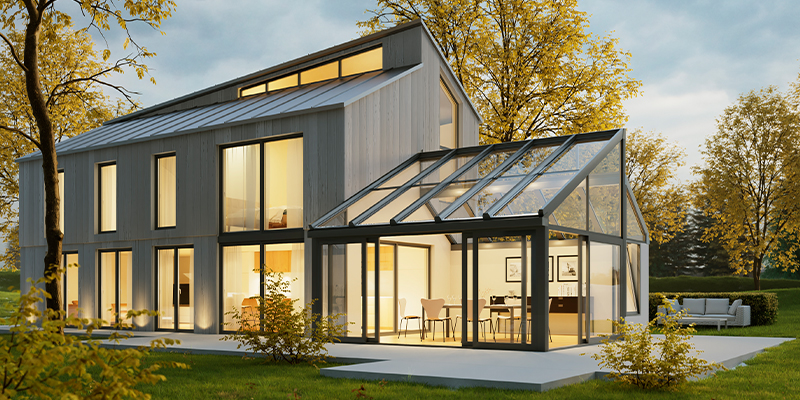 Moderner Wintergarten aus Aluminium und Glas an einem Einfamilienhaus mit großer Fensterfront und Blick in den herbstlichen Garten.