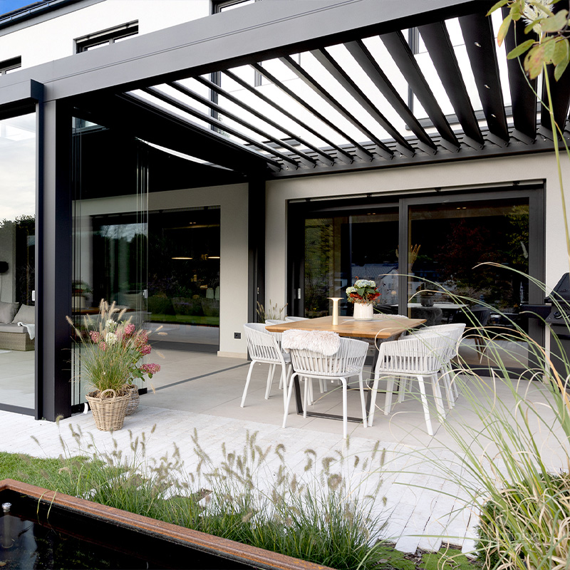 Modernes Lamellendach mit seitlichen Glaselementen über einer Terrasse mit Esstisch
