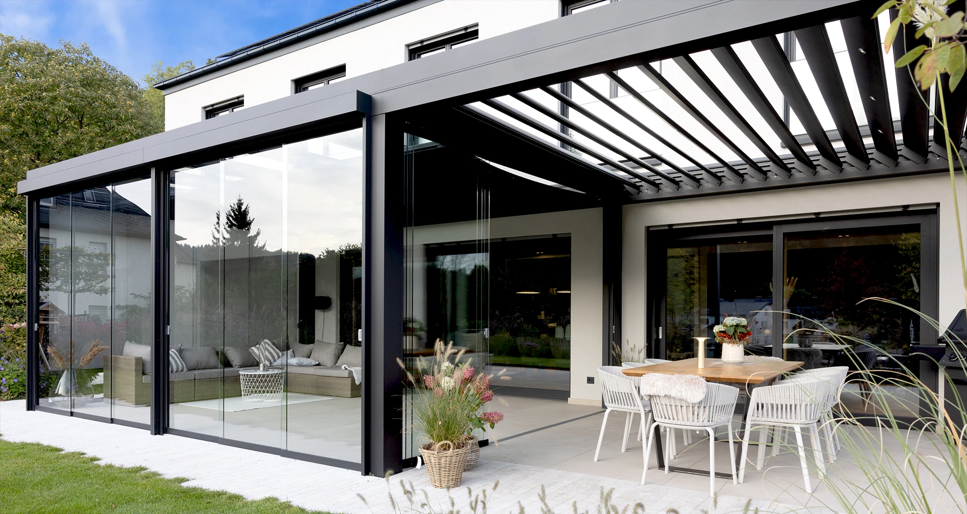 Moderner Sommergarten mit Glaswänden und stimmungsvoller LED-Beleuchtung bei Sonnenuntergang, eingerichtet mit gemütlichen Rattanmöbeln.