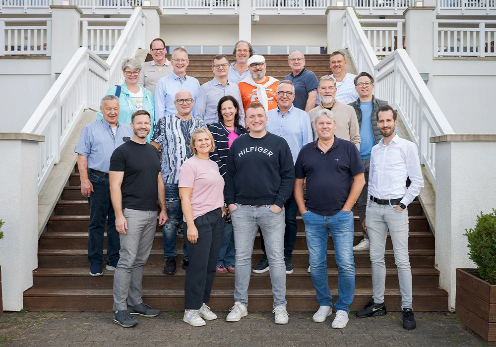 Gruppe von Männern und Frauen steht gemeinsam auf einer Außentreppe vor einem Gebäude mit weißem Geländer