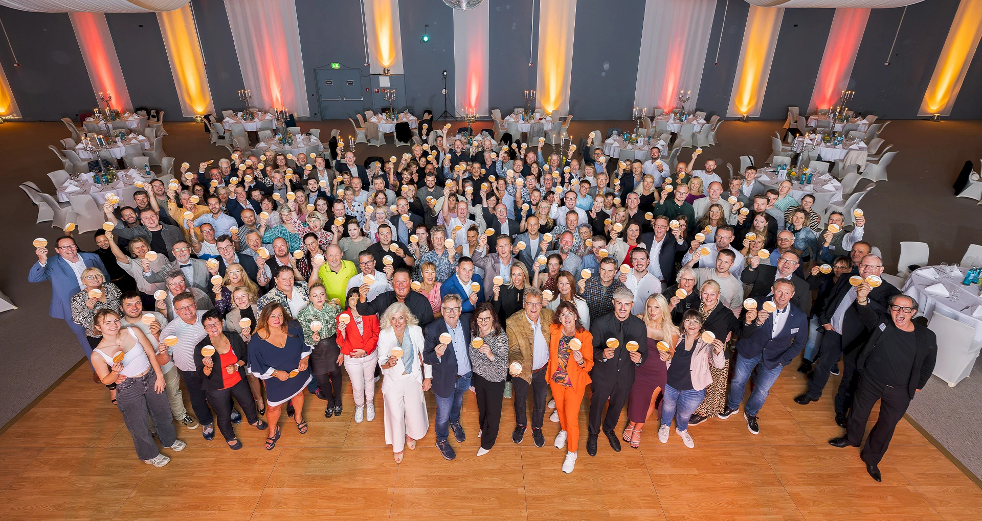Mehrere hundert Personen stehen dicht zusammen in einem Veranstaltungssaal und halten runde Sonne am Haus Bierdeckel hoch